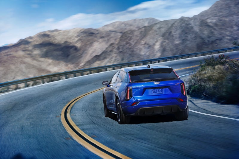 Rear View of a Blue 2026 OPTIQ-V Driving on a Curve of a Mountain Row | Corwin Cadillac Reno in Reno NV